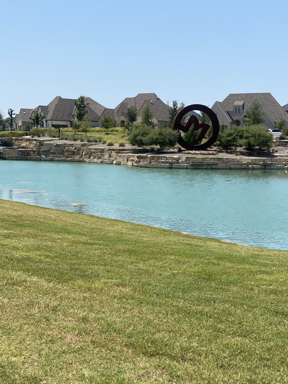 M3 Ranch monument entrance in Mansfield, TX — stone 'M' medallion with pond and community rooftops in the background