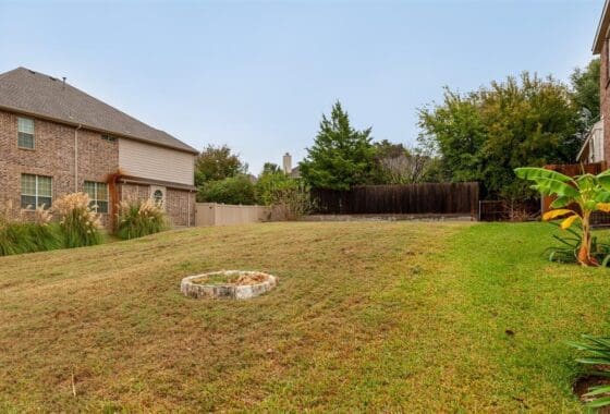 Backyard with grass, fence, and a house.