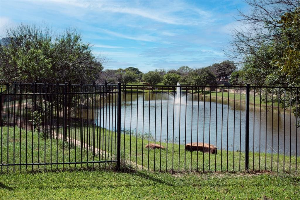 Black metal fence overlooking a pond with a fountain.